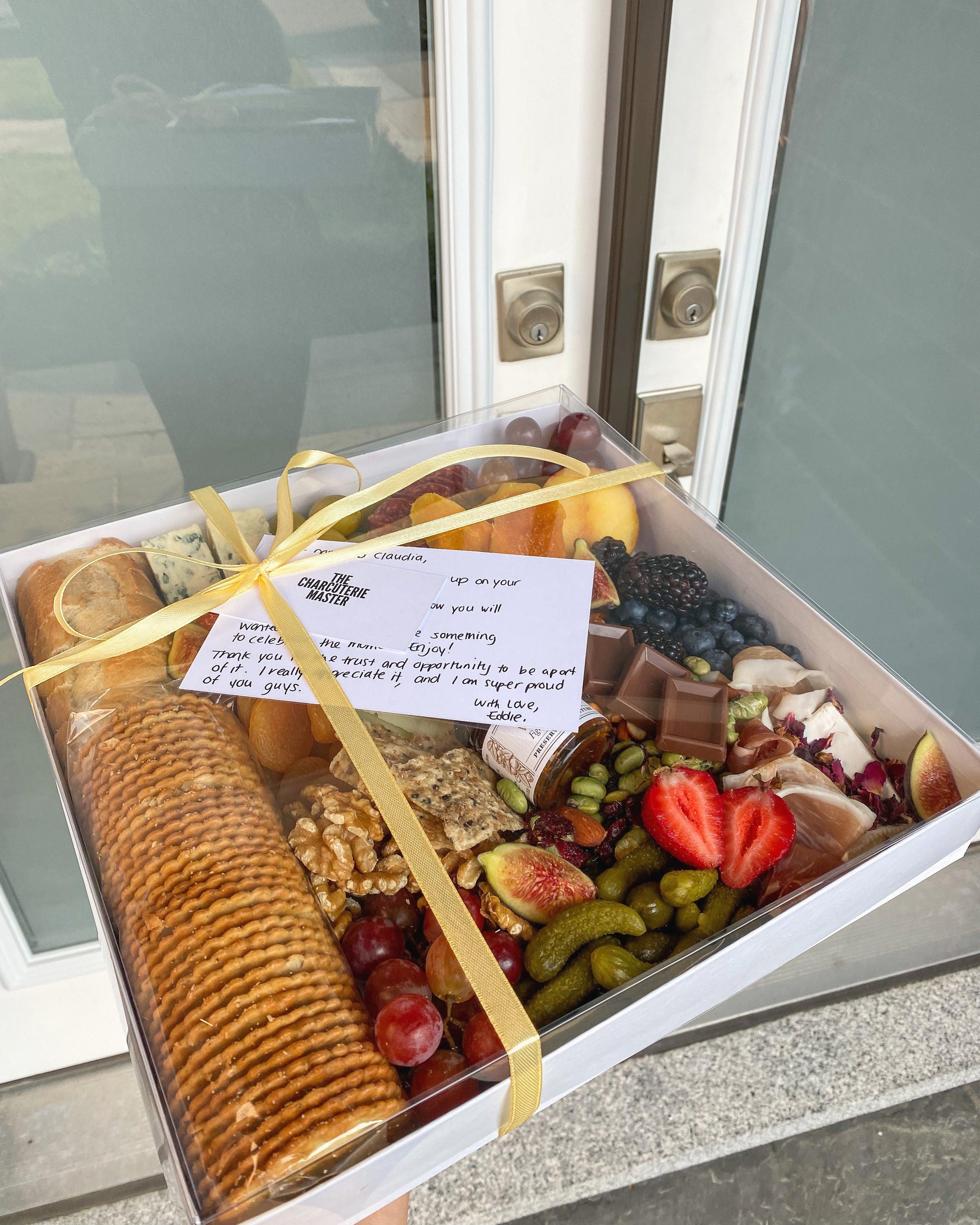 A large premium charcuterie box delivered to a doorstep with a handwritten note