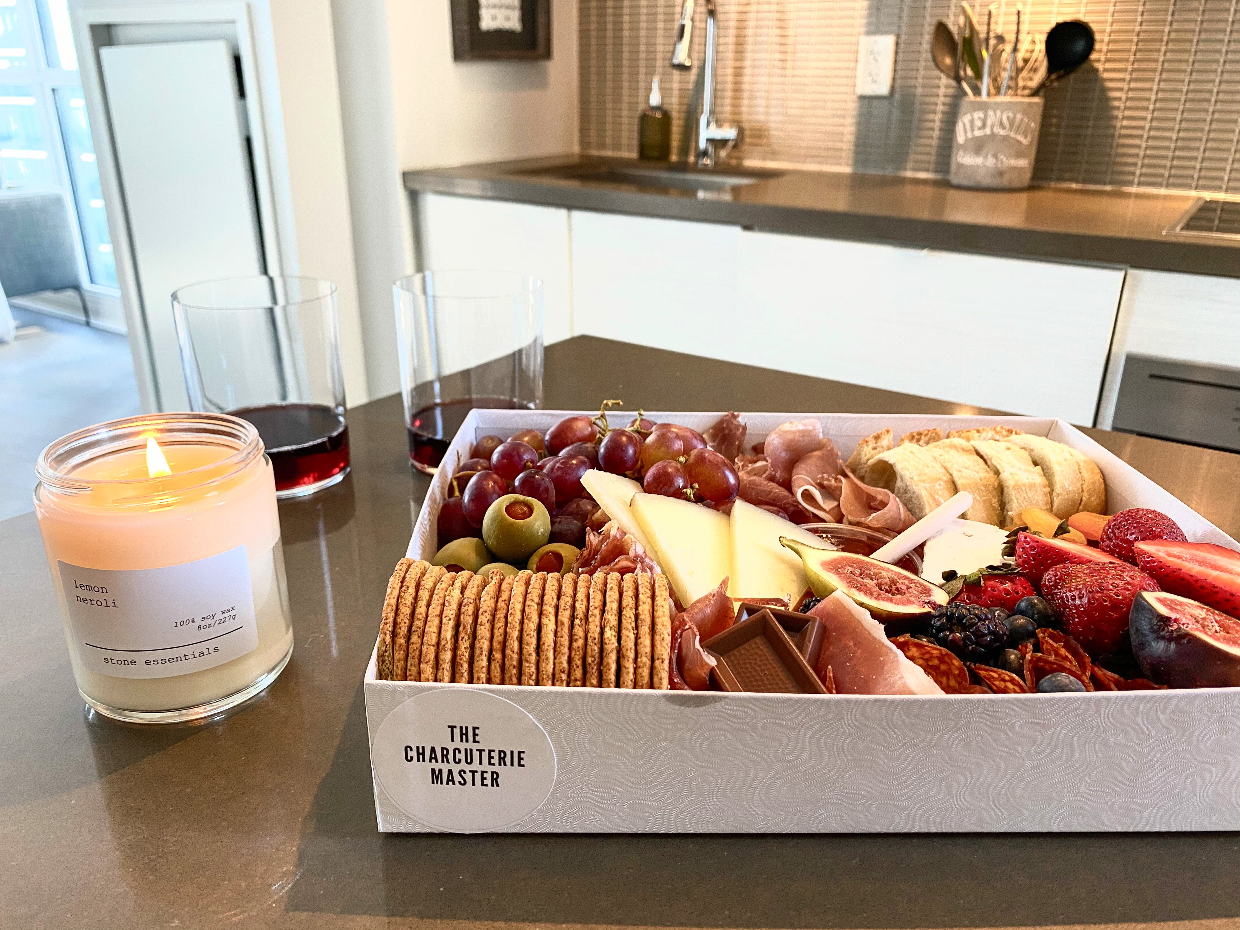 A beautifully arranged charcuterie box with cheeses, cured meats, fruit and crackers beside a glass of wine